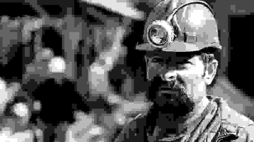Black and white photo of a miner wearing a construction hat with a light