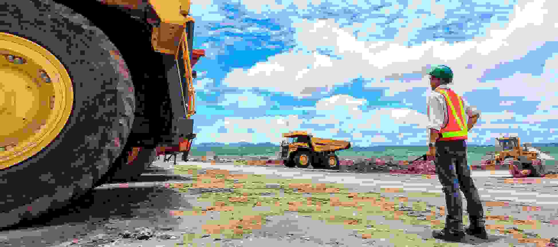 Construction worker at an extraction site surrounded by large vehicles